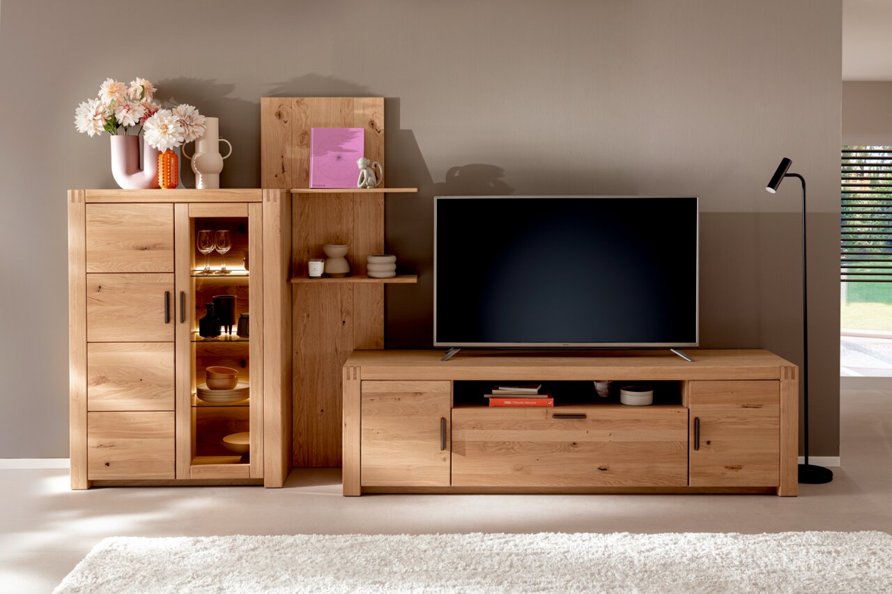 Helles Holz-Highboard mit Glastür und Regalen, dekoriert mit Vasen und Blumen, in einem modernen Wohnzimmer. Perspektive von vorne.