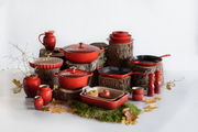 Roter ovaler Bräter mit Deckel, umgeben von passendem Kochgeschirr, aus einer leicht erhöhten Perspektive fotografiert.