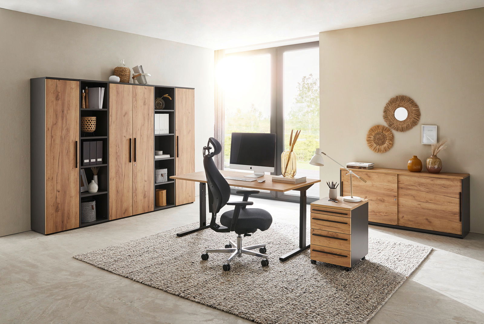 Moderne Büromöbel in einem hellen Raum mit Schreibtisch, Rollcontainer und Aktenschränken in Holzoptik, seitliche Perspektive.