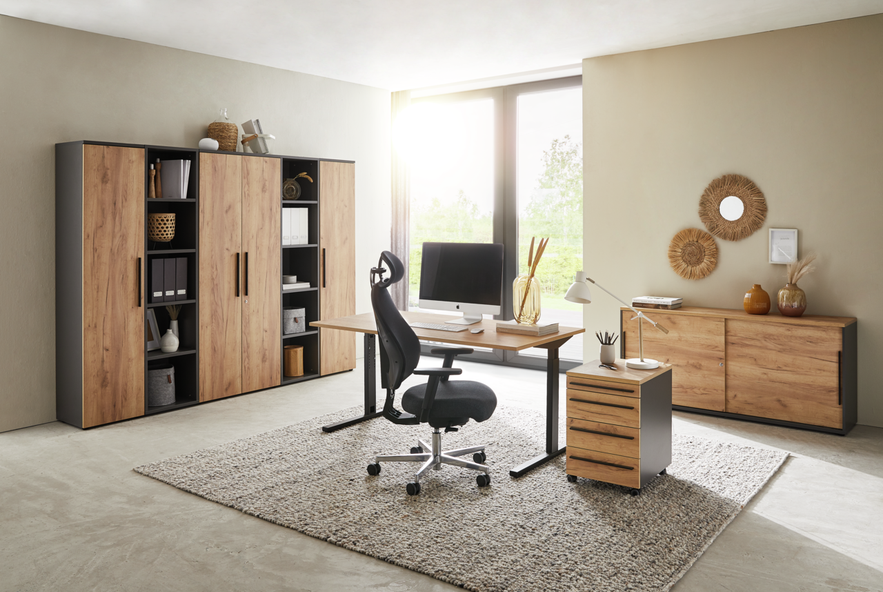 Moderne Büromöbel in einem hellen Raum mit Schreibtisch, Rollcontainer und Aktenschränken in Holzoptik, seitliche Perspektive.