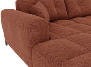 Nahaufnahme eines rostbraunen, gepolsterten Sofas mit strukturierter Stoffoberfläche, breiter Armlehne und gesteppter Sitzfläche; Perspektive: schräg von vorne links