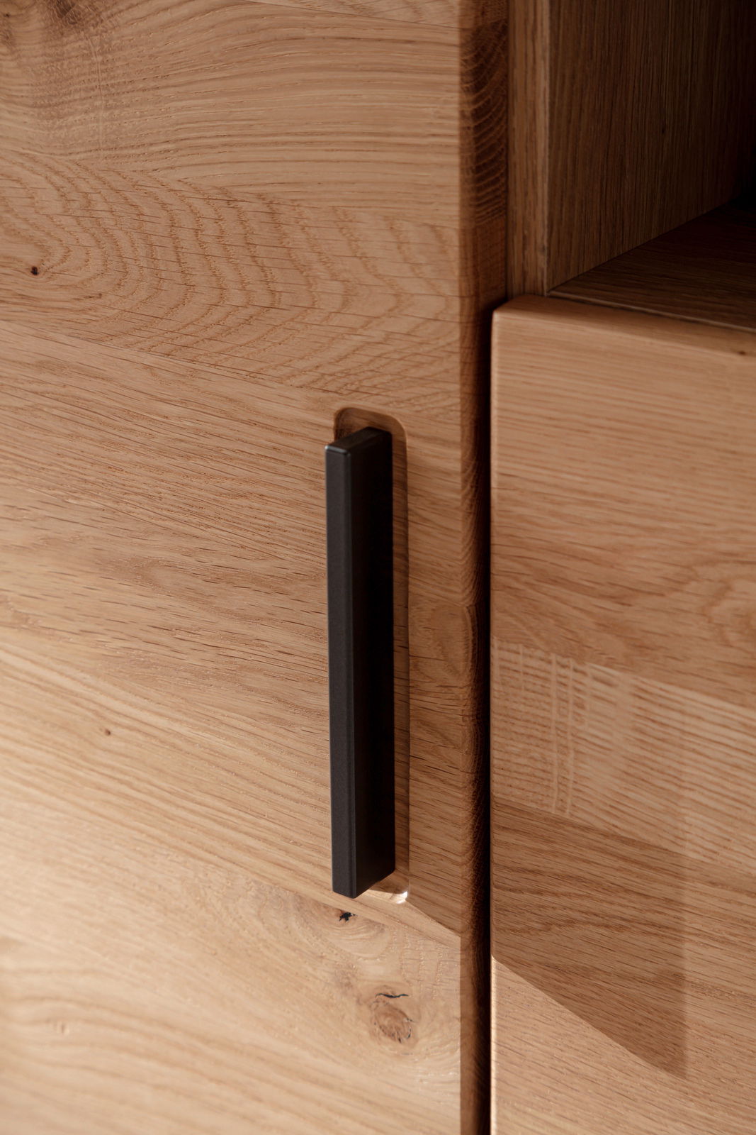 Nahaufnahme eines Highboards aus Holz mit schwarzem Griff, seitliche Perspektive