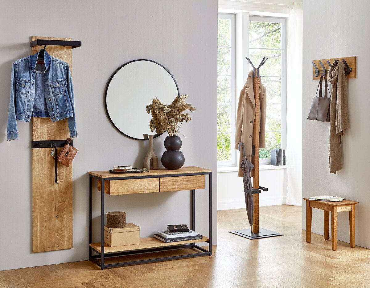 Modern eingerichteter Flur mit Garderobenmöbeln aus Holz und schwarzem Metall: Wandgarderobe mit Jeansjacke, Konsole mit rundem Spiegel und Deko, freistehender Garderobenständer mit Mantel und Schirm sowie Wandhakenleiste mit Tasche und Schal; Perspektive