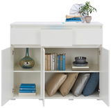 Weißes Sideboard mit zwei offenen Türen, gefüllt mit Büchern, Kissen und Dekorationen, aus frontaler Perspektive.