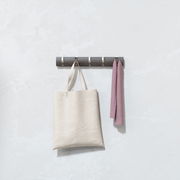 Wandgarderobe mit mehreren Haken, an denen eine beige Tasche und ein rosa Tuch hängen, seitliche Perspektive