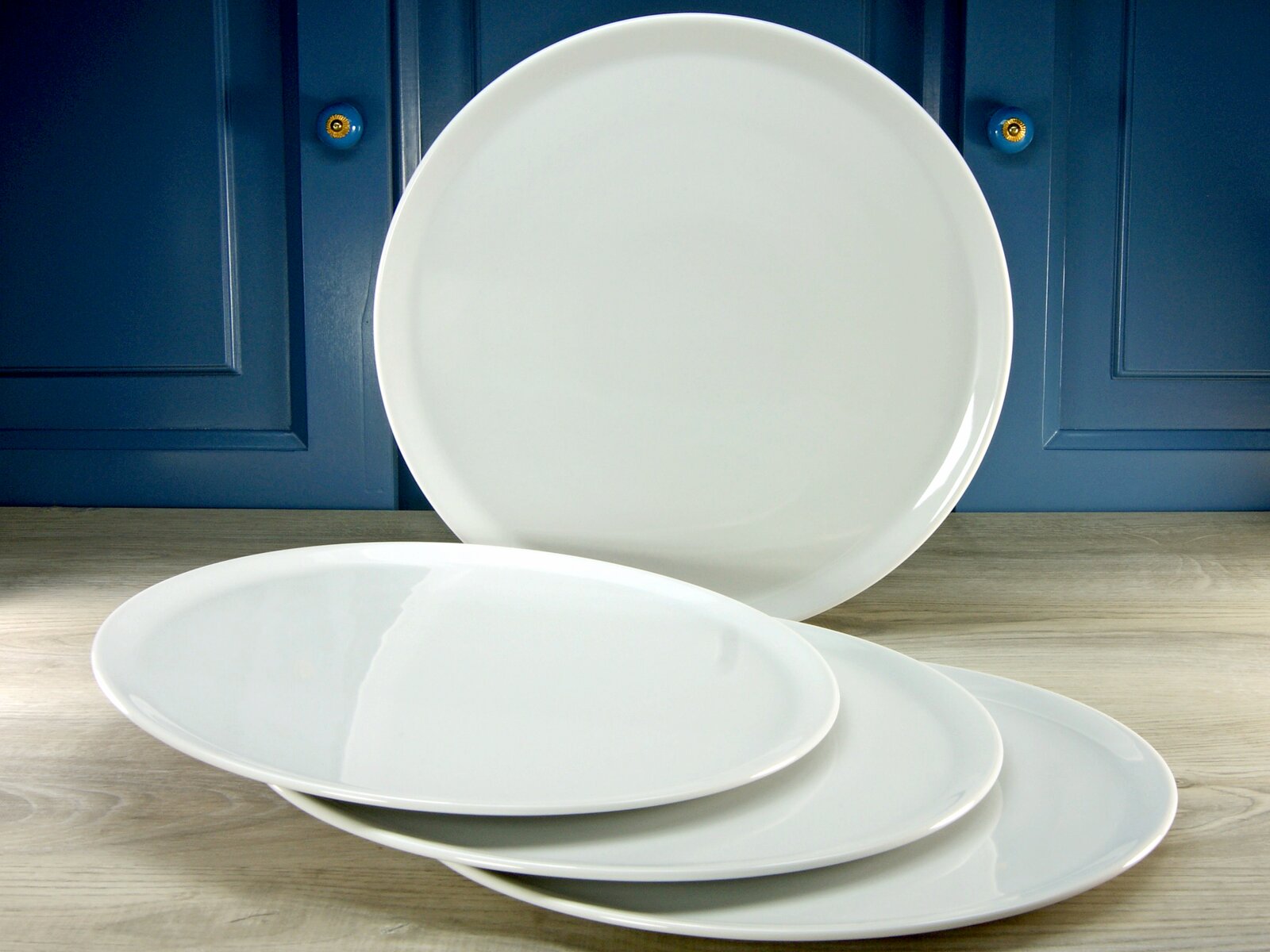 Creatable Pizzateller 4-tlg EUROPA Vier weiße Pizzateller, einer aufrecht stehend und drei flach liegend, vor einem blauen Hintergrund.