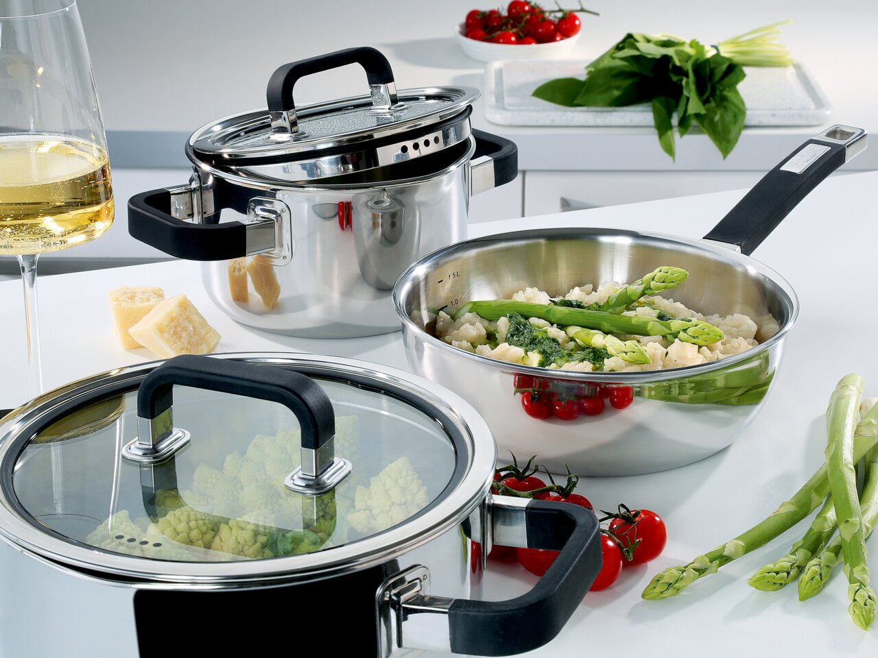 Topf-Set FUSION2+ 5-teilig aus Edelstahl, gefüllt mit frischen Zutaten wie Spargel und Tomaten, in einer modernen Küchenumgebung, seitliche Perspektive.
