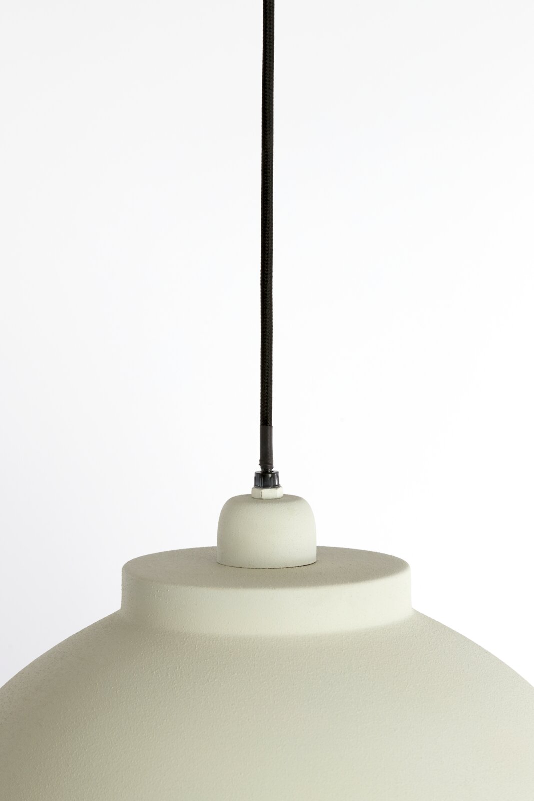 Close-up van een hanglamp met een zwarte kabel en een crèmekleurige lampenkap, gezien van bovenaf.