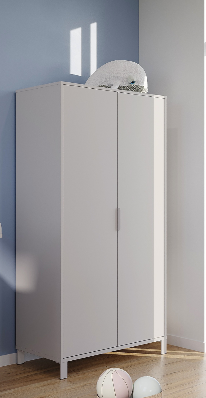 Moderner weißer Kleiderschrank mit zwei Türen, seitliche Perspektive, auf hellem Holzboden vor blauer Wand, mit Plüschtier obenauf.