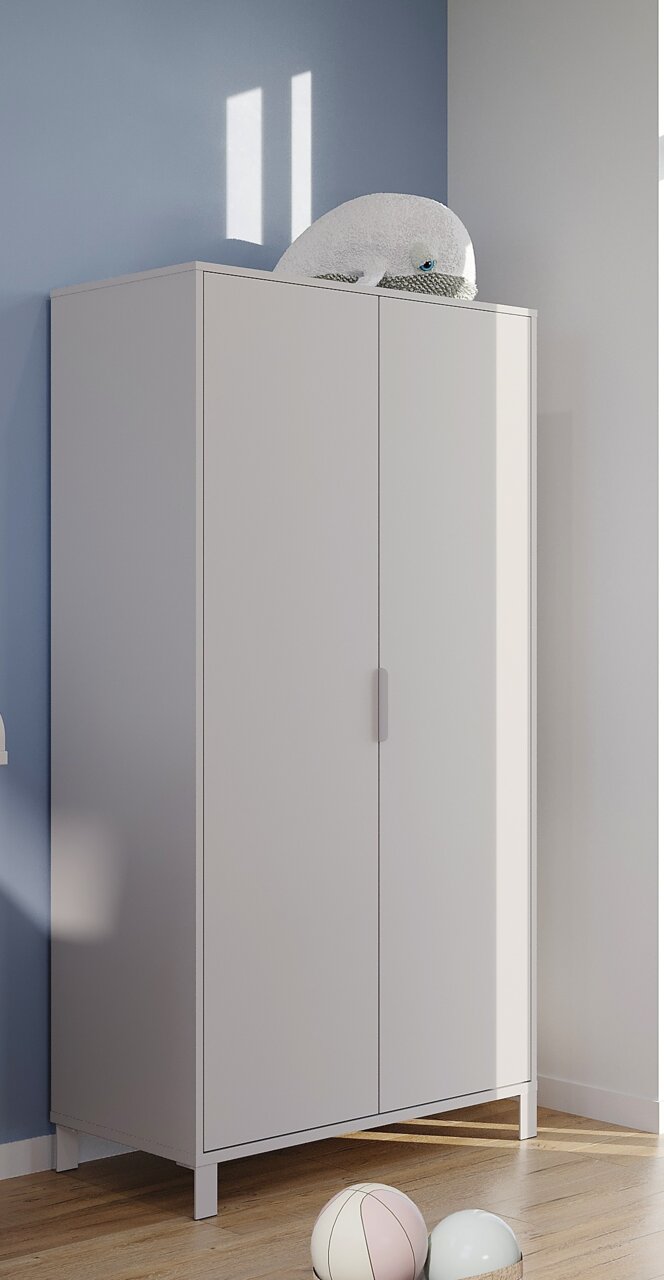 Moderner weißer Kleiderschrank mit zwei Türen, seitliche Perspektive, auf hellem Holzboden vor blauer Wand, mit Plüschtier obenauf.
