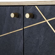 Nahaufnahme einer Kommode mit dunkler, strukturierter Oberfläche und goldenen Griffen sowie diagonalen Zierleisten, von vorne betrachtet.