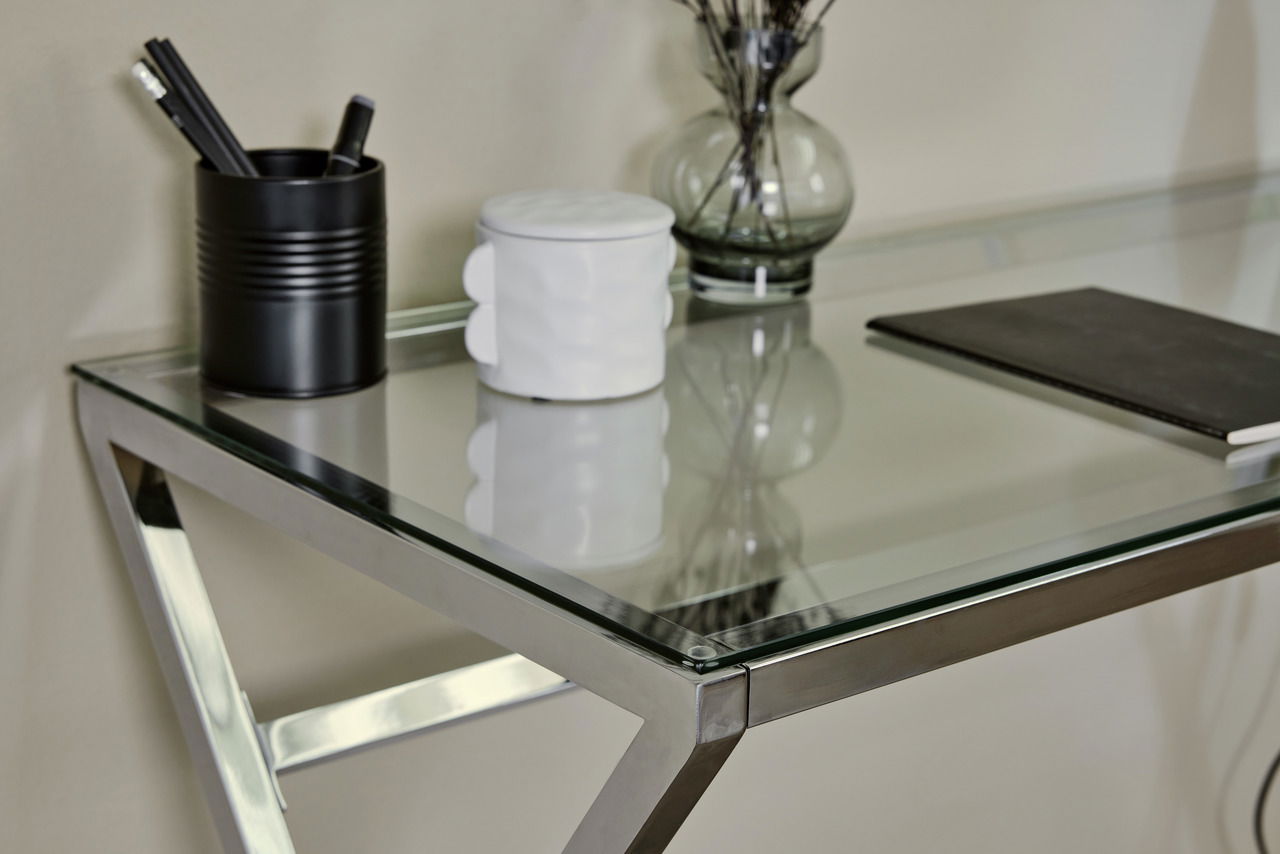 Moderner Schreibtisch mit Glasplatte und Metallrahmen, seitliche Perspektive, mit Stiftehalter, Vase und Notizbuch.