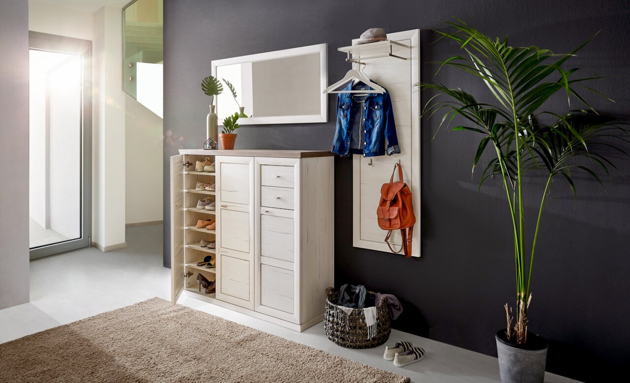 Hom´in Schuhschrank CAMRON Heller Flur mit einem weißen Schuhschrank und Garderobenpaneel, dekoriert mit Pflanzen und Accessoires, seitliche Perspektive.