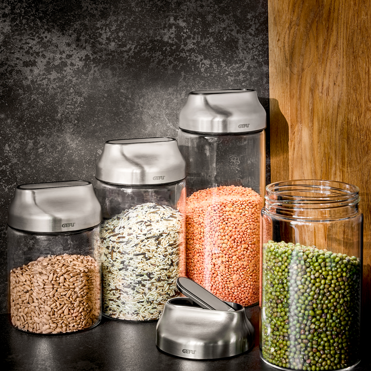 Vorratsdosen aus Glas mit Edelstahl-Deckeln, gefüllt mit verschiedenen Lebensmitteln, aus seitlicher Perspektive fotografiert.