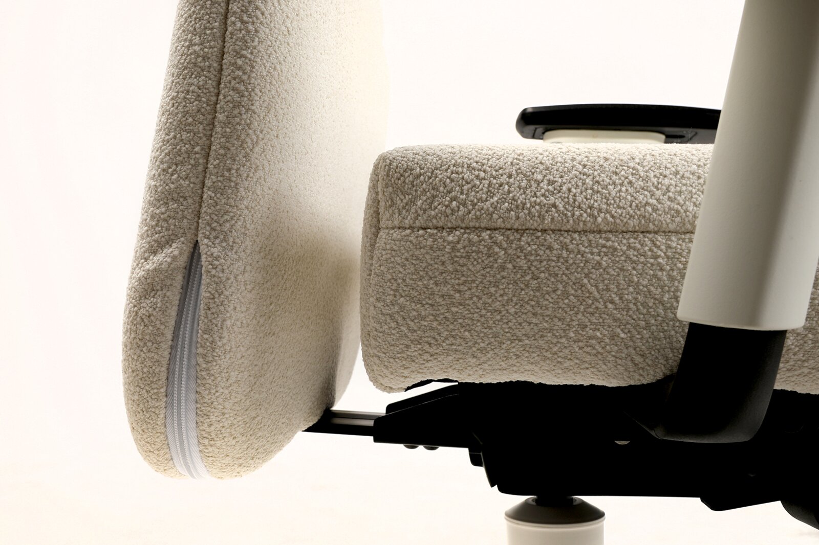 Detailaufnahme eines ergonomischen Bürostuhls mit beigem Bouclé-/Teddybezug, Seitenansicht mit sichtbarer Sitzfläche, Rückenlehne und Armlehne vor hellem Hintergrund