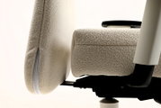 Detailaufnahme eines ergonomischen Bürostuhls mit beigem Bouclé-/Teddybezug, Seitenansicht mit sichtbarer Sitzfläche, Rückenlehne und Armlehne vor hellem Hintergrund