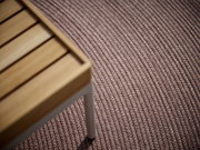 Nahaufnahme eines Outdoor-Teppichs mit strukturierter Oberfläche und einem Teil eines Holztisches in der linken oberen Ecke.