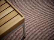 Nahaufnahme eines Outdoor-Teppichs mit strukturierter Oberfläche und einem Teil eines Holztisches in der linken oberen Ecke.