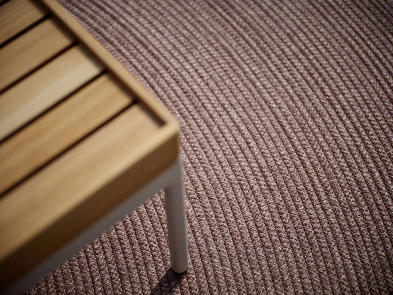 Close-up van een buitentapijt met een gestructureerd oppervlak en een deel van een houten tafel in de linkerbovenhoek.