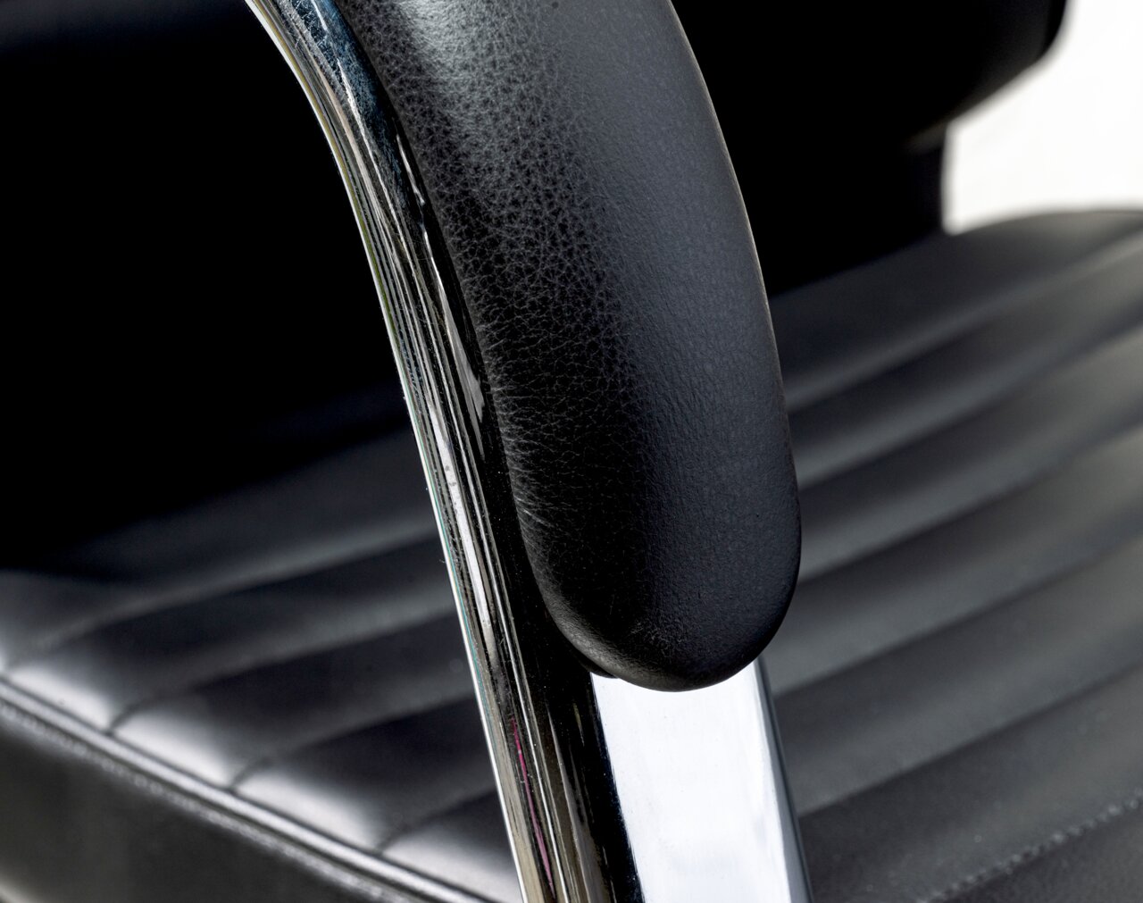 Nahaufnahme eines schwarzen Schwingstuhls mit gepolstertem Sitz und Armlehne aus Leder, seitliche Perspektive