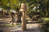 Outdoor-Stehleuchte aus Rattan in einem tropischen Garten, frontal fotografiert.