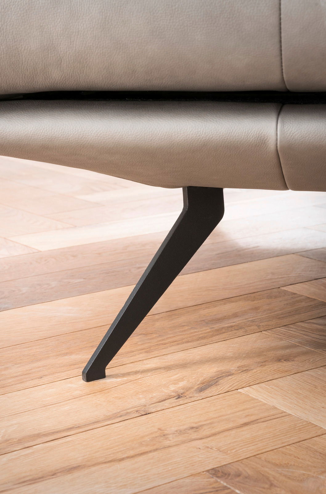 Nahaufnahme eines modernen Sofafußes aus Metall auf einem Holzboden, seitliche Perspektive