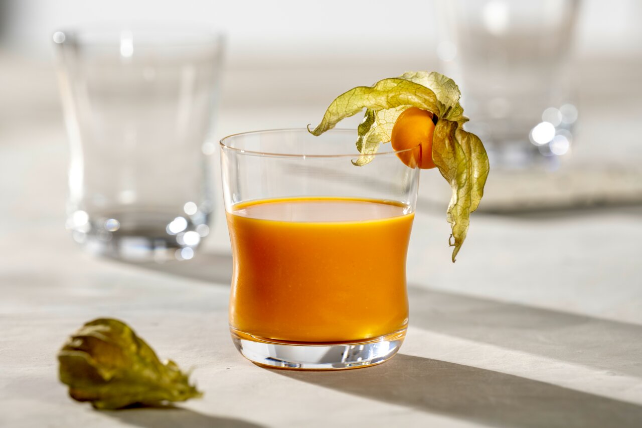 Ein elegantes Glas mit 330 ml Fassungsvermögen, gefüllt mit einem orangefarbenen Getränk, dekoriert mit einer Physalis, aus der Seitenperspektive fotografiert.