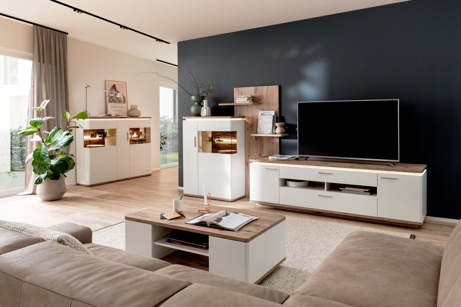 Modernes Wohnzimmer-Set in Weiß und Holzoptik mit TV-Lowboard, Vitrine und Couchtisch vor dunkelblauer Akzentwand, seitliche Perspektive aus Sitzhöhe