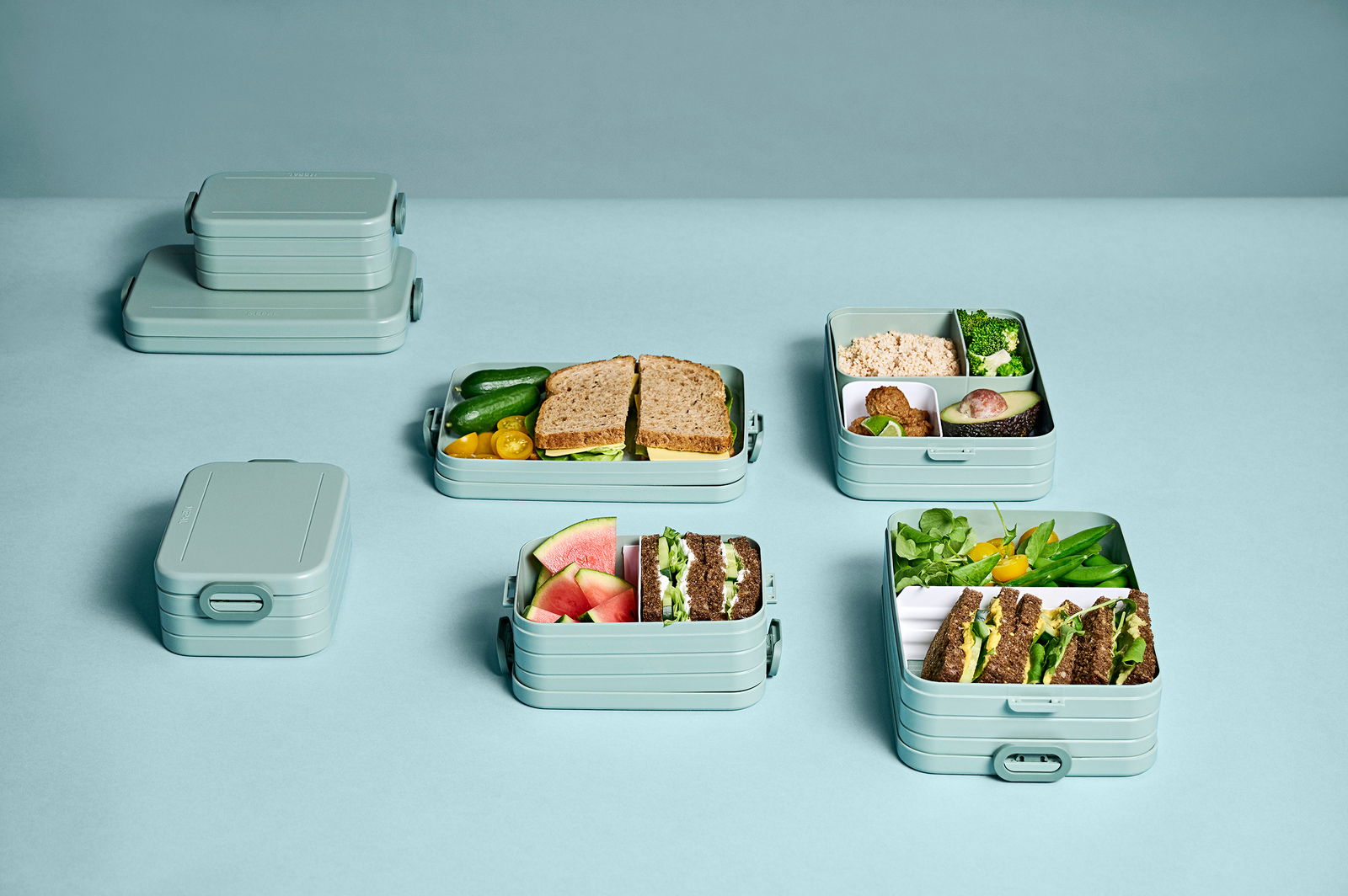Mehrere Bento-Lunchboxen in verschiedenen Größen, gefüllt mit Sandwiches, Gemüse und Obst, aus der Vogelperspektive fotografiert.