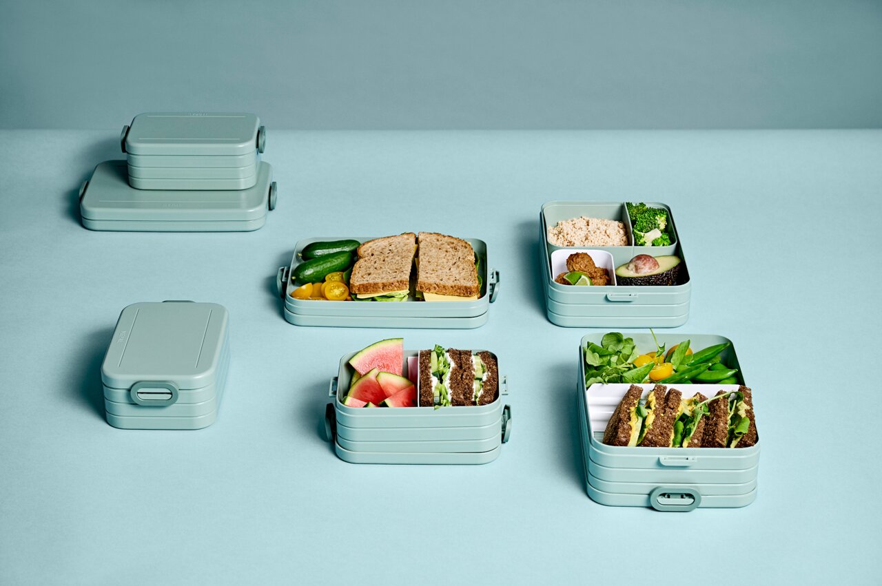 Mehrere Bento-Lunchboxen in verschiedenen Größen, gefüllt mit Sandwiches, Gemüse und Obst, aus der Vogelperspektive fotografiert.