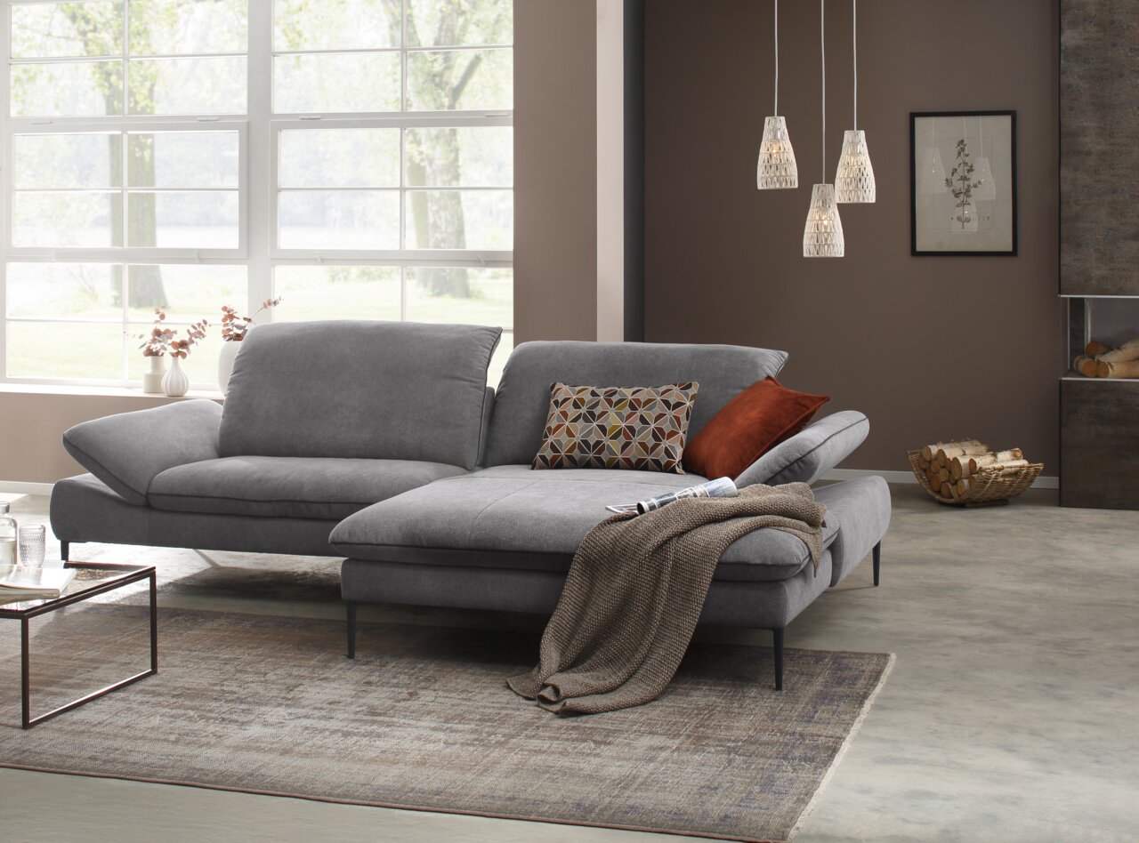 Grijze longchair-set in een moderne woonkamer, met sierkussens en een deken, gezien vanuit het perspectief linksvoor.