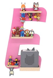 Frontalansicht: Große rosafarbene Dekoration in Form des Buchstabens E mit mehreren kleinen Spielfiguren auf Holzleisten; unten ein grauer Würfel-Lautsprecher mit Katzenmotiv auf Holzsockel.