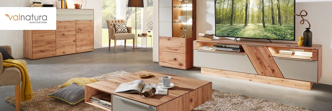 Ein gemütliches Wohnzimmer mit Holzmöbeln, Teppich und einem großen Fernseher an der Wand.