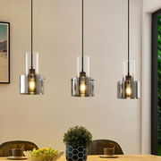 Drei moderne Hängeleuchten mit transparenten Glasschirmen, die von der Decke über einem Esstisch hängen. Perspektive: Frontalansicht.