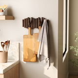 Wandgarderobe mit Holzstäben und Haken, an der zwei Schneidebretter und ein Handtuch hängen, seitliche Perspektive.