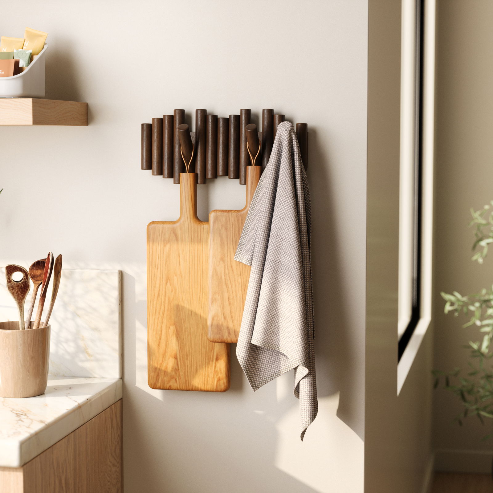Wandgarderobe mit Holzstäben und Haken, an der zwei Schneidebretter und ein Handtuch hängen, seitliche Perspektive.