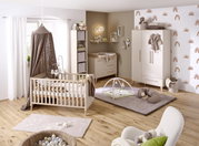 Ein gemütliches Babyzimmer mit einem Babybett aus Holz, umgeben von sanften Farben und dekorativen Elementen. Die Perspektive zeigt das Zimmer von vorne, mit einem Blick auf das Bett, einen Kleiderschrank und eine Wickelkommode.