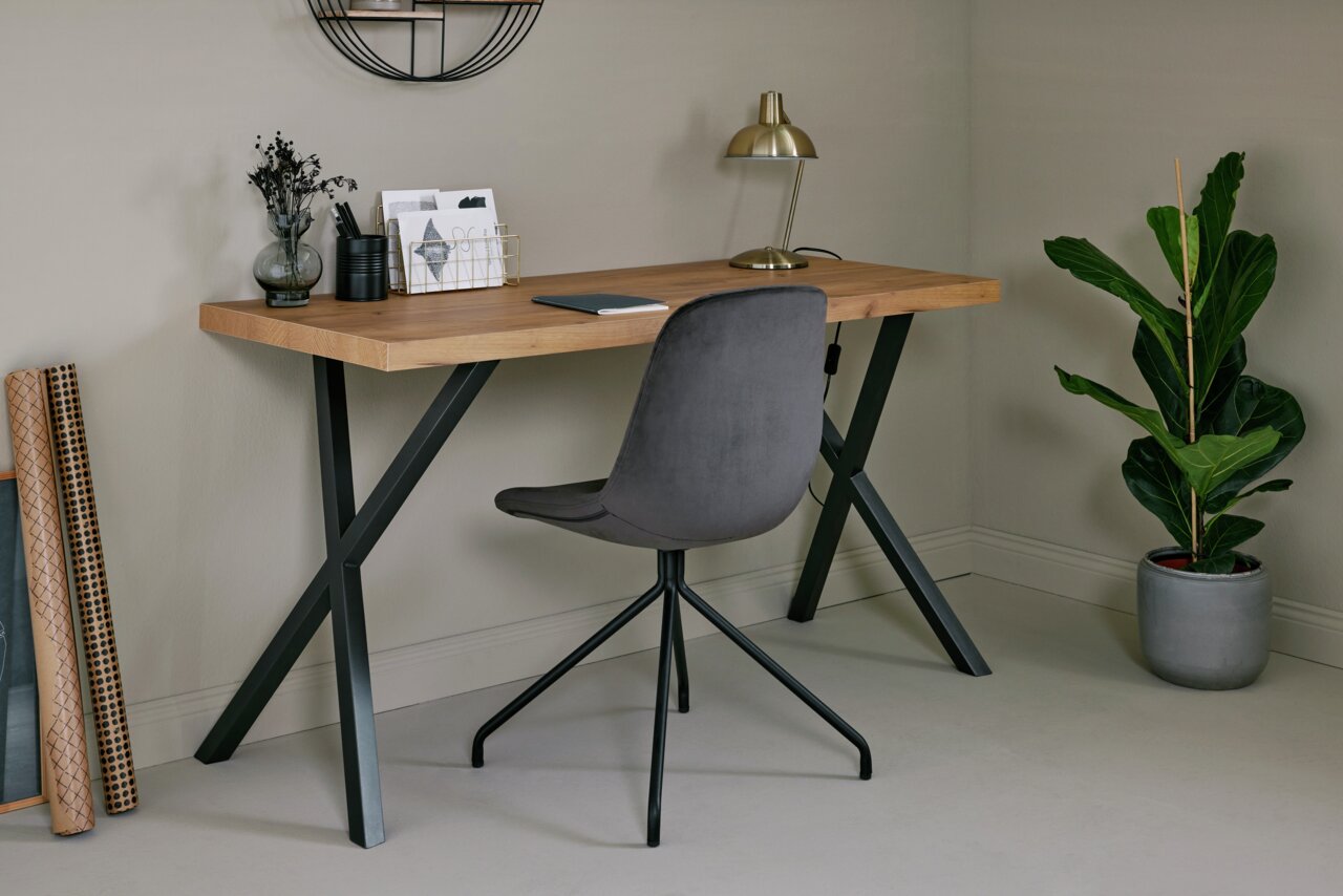 Moderner Schreibtisch mit Holzplatte und schwarzen Metallbeinen, seitliche Perspektive, dekoriert mit Lampe, Pflanzen und Schreibutensilien.