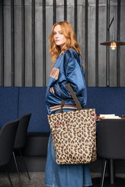 Frau in blauer Jacke mit einer Leo-Muster Einkaufstasche, seitliche Perspektive