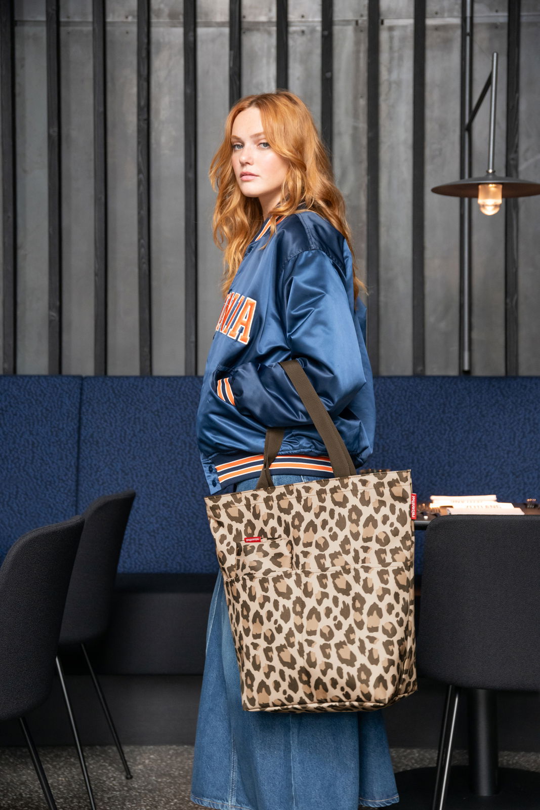 Frau in blauer Jacke mit einer Leo-Muster Einkaufstasche, seitliche Perspektive