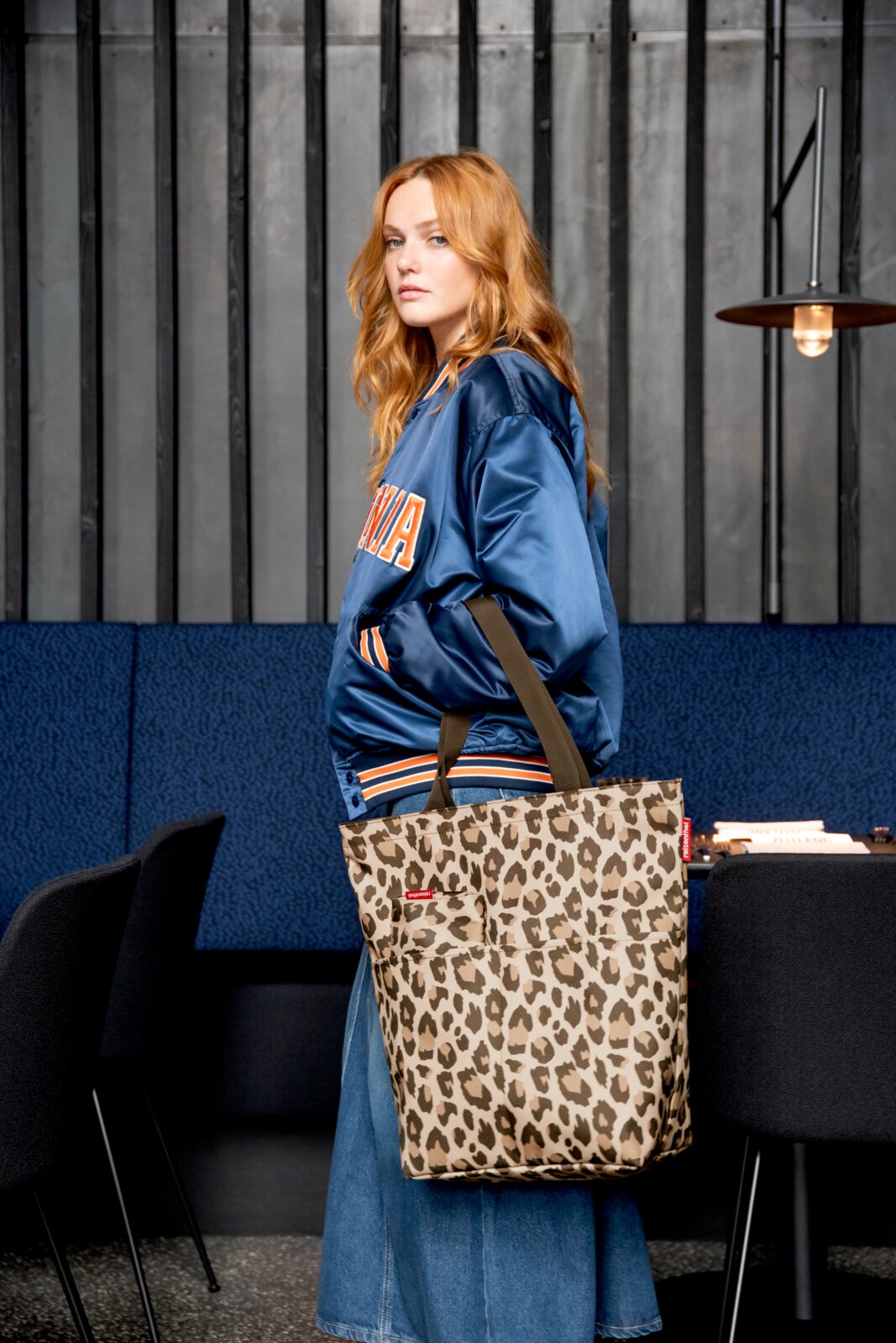 Frau in blauer Jacke mit einer Leo-Muster Einkaufstasche, seitliche Perspektive