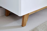 Nahaufnahme eines weißen Sideboards mit Holzbeinen, Perspektive von unten.