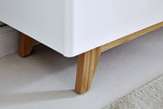Nahaufnahme eines weißen Sideboards mit Holzbeinen, Perspektive von unten.