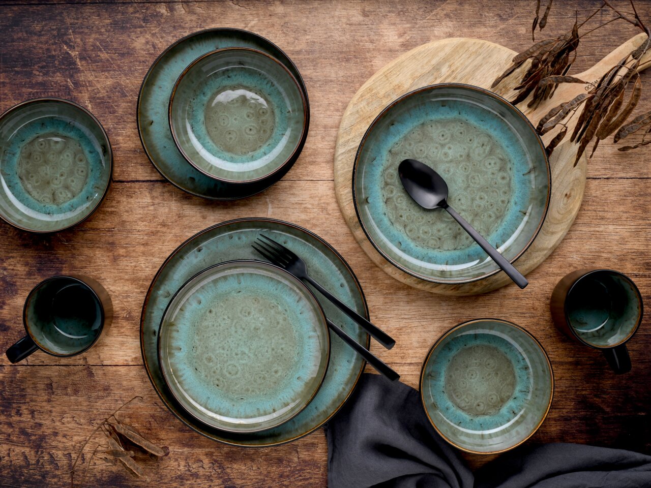 Kombiservice 30-delig Green, vanuit vogelperspectief gerangschikt op een houten tafel, bestaande uit borden, schalen en kopjes in een groen ontwerp met zwart bestek.