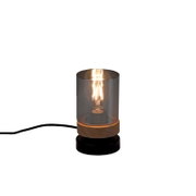 Moderne Tischlampe mit rauchgrauem Glaszylinder, sichtbarer leuchtender Filament-Glühbirne und Holzsockel auf grauem Untergrund, Frontansicht leicht von oben