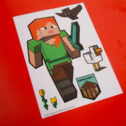 Schräg von oben fotografierter Minecraft-Stickerbogen auf rotem Hintergrund mit der Figur Alex mit Diamantschwert sowie Fledermaus, Huhn, Sonnenblume und Crafting-Table-Motiv.