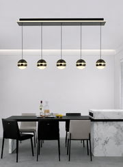 Moderne LED-Pendelleuchte mit fünf kugelförmigen Lampen, hängend über einem Esstisch in einem stilvollen Esszimmer, seitliche Perspektive.
