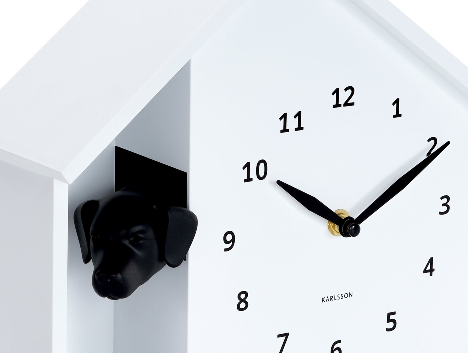 Weiße Wanduhr mit schwarzem Hundekopf, der aus einer Öffnung an der Seite herausschaut. Die Uhr hat ein minimalistisches Design mit schwarzen Zeigern und Zahlen. Perspektive von schräg vorne.