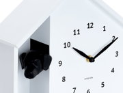 Weiße Wanduhr mit schwarzem Hundekopf, der aus einer Öffnung an der Seite herausschaut. Die Uhr hat ein minimalistisches Design mit schwarzen Zeigern und Zahlen. Perspektive von schräg vorne.