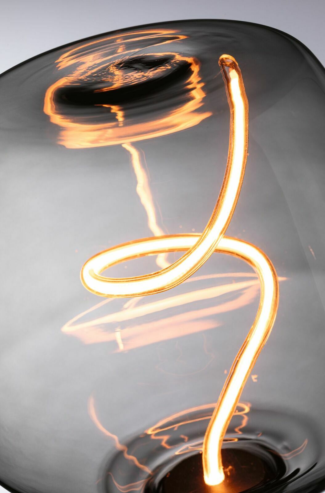 Nahaufnahme einer leuchtenden LED-Glühbirne mit geschwungenem Filament, seitliche Perspektive